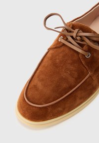 Brown suede shoe with a rounded toe, lace-up design, and subtle stitching detail along the edge. Rubber sole with a slight beige accent.