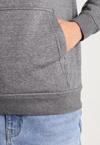 Grå sweatshirts med en framficka, ribbad mudd och nederkant, tillverkad av mjukt tyg, i kombination med ljusblå jeans.