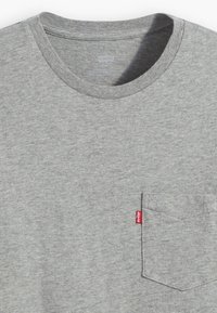 Grå kortærmet T-shirt lavet af bomuld; har en rund hals og en lomme på venstre bryst med et rødt label-logo. Blød tekstur.