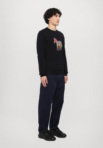 Black sweatshirt featuring a colorful embroidered horse design, paired with navy pants and black shoes, shown on a standing male model.
