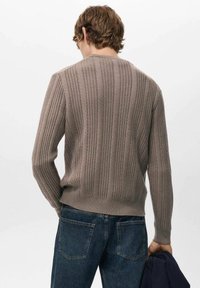 Bruine geribbelde gebreide trui met een gestructureerd patroon en een ronde halslijn. Gecombineerd met donkerblauwe denim jeans. Geen zichtbare logo's of afbeeldingen.