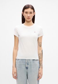 Hvit bomulls t-skjorte med rund hals og korte ermer. Har en liten logo på brystet. Kombinert med lyseblå denim jeans.