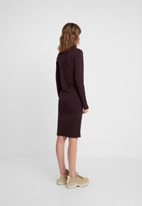 Langarm, aansluitend jurkje van donkerpaarse jersey stof, kniehoogte, gecombineerd met beige schoenen met gestructureerde zolen.
