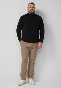 Schwarzer Rollkragenpullover, beige Hose und weiße Turnschuhe. Der Pullover ist eng anliegend und die Hose hat eine feine Textur.
