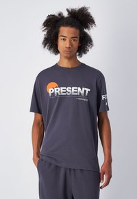 Camiseta de algodón gris de manga corta, con gráfico de "PRESENT" en blanco y naranja, y diseño minimalista. Tejido texturizado.