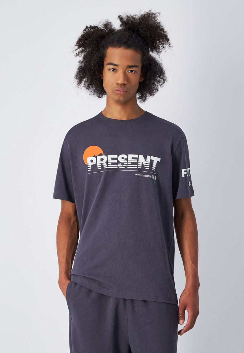 Camiseta de algodón gris de manga corta, con gráfico de "PRESENT" en blanco y naranja, y diseño minimalista. Tejido texturizado.