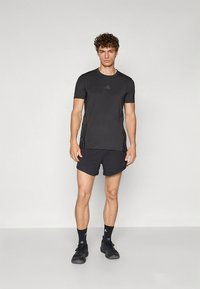 Maglietta atletica nera e pantaloncini realizzati in tessuto leggero, caratterizzati da scollo rotondo, maniche corte e tre strisce orizzontali su ciascun lato.