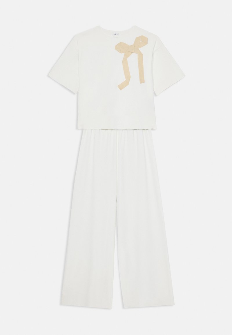 Conjunto branco de duas peças com uma blusa de mangas curtas com um detalhe de laço bege e calças de perna larga com uma cintura elástica. Textura suave.