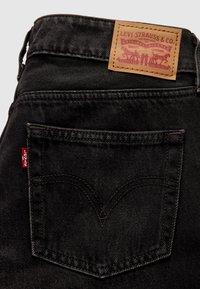 Poche arrière d’un jean Levi’s noir avec une étiquette rouge Levi’s et un patch en cuir beige avec le logo et le design de la marque.