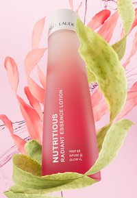 Rosa gradientflaske med frostet finish, merket "NUTRITIOUS RADIANT ESSENCE LOTION." Omgitt av rosa blader og grønt løvverk.