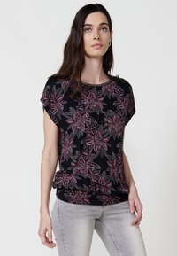 Blouse noire avec un motif floral rose, manches courtes et une taille froncée. Fabriquée en tissu doux avec une texture lisse.
