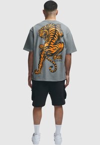 Grå t-skjorte med korte ermer og stort oransje tigermotiv på ryggen, kombinert med svarte cargo-shorts og hvite joggesko.