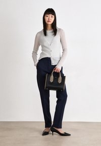 Light gray ribbed cardigan over a gray top, paired with navy tailored pants and black pointed heels. A black handbag with tan accents is held.