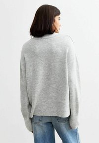 Pull en tricot gris clair avec une coupe décontractée, des poignets côtelés et un col haut. Porté avec un jean en denim bleu.