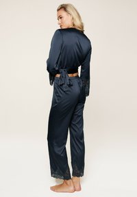 Navy satijnen pyjama set met lange mouwen met kantaccenten, knopen en een broek met wijde pijpen met vergelijkbare kantversiering aan de zoom.