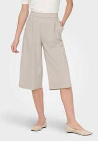 Beżowe spodnie culotte z wysokim stanem, z bocznymi kieszeniami i szerokimi nogawkami. Gładka faktura i dopasowany wygląd.