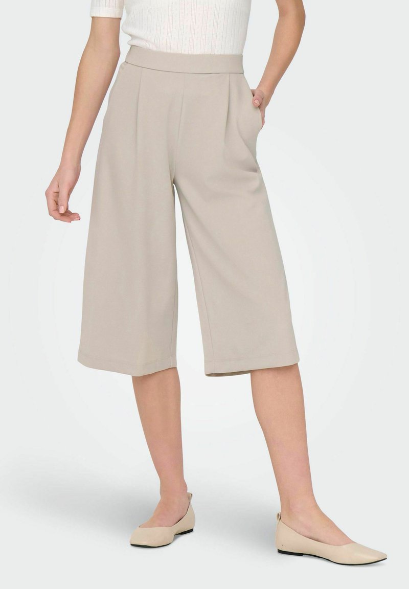 Beżowe spodnie culotte z wysokim stanem, z bocznymi kieszeniami i szerokimi nogawkami. Gładka faktura i dopasowany wygląd.