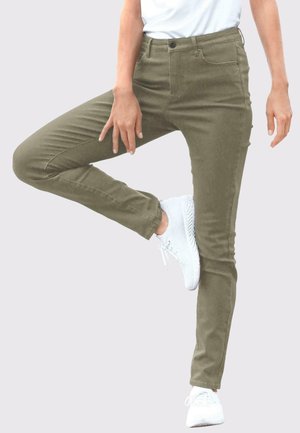Olivgrüne Slim-Fit-Hosen mit glatter Textur, Fünf-Taschen-Design und vorderen Nähdetails, kombiniert mit weißen Sportschuhen.