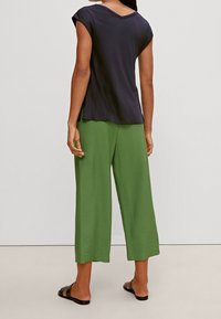 Top blu navy scuro a maniche corte con scollo a V, abbinato a pantaloni verdi larghi e ampi in tessuto leggero. Sandali neri piatti.