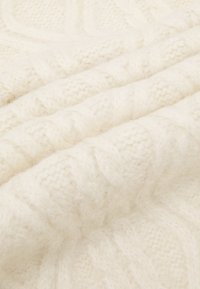 Tessuto lavorato a maglia color crema con un motivo a treccia testurizzato, caratterizzato da fibre morbide e soffici e un aspetto liscio e caldo.