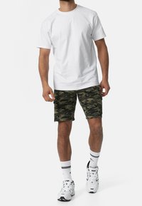 Witte t-shirt met korte mouwen, gecombineerd met camouflagemotief shorts in groentinten, aangevuld met witte sneakers en gestreepte sokken.