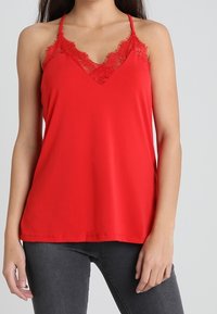 Rode mouwloze top met een V-hals en kantdetails rond de halslijn. Glad stof, losse pasvorm en eenvoudig ontwerp.