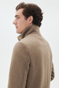 Manteau en laine marron avec un col haut, présentant une texture lisse et une coupe ajustée. Vue de profil montrant la silhouette cintrée et les détails de couture.
