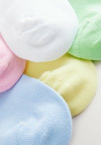 Chaussettes en coton colorées pour la cheville, de couleur rose, blanche, bleue, jaune et verte, avec une texture lisse et des bords arrondis, empilées.