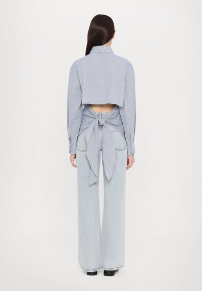 Kuttet blå skjorte med lange ermer, åpen rygg bundet i livet, paret med høyt liv lyse denim vide bukser.