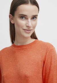 Pulover tricotat portocalie cu guler rotund. Materialul pare moale și texturat, având un tipar delicat de heather. Design simplu, clasic.