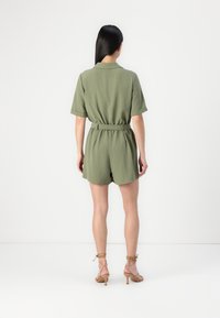 Une combinaison verte olive à manches courtes avec une taille ceinturée et une coupe décontractée. Présente une texture douce et un col.