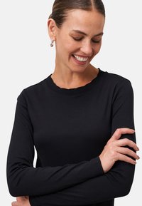 Zwarte lange mouwen top met een scalloped halslijn, met een gladde textuur en een getailleerd ontwerp. De mouwen zijn licht taps toelopend bij de polsen.