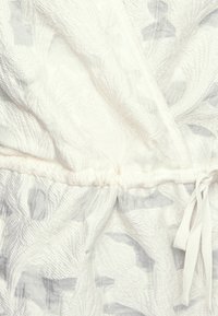 Tecido branco texturizado com um padrão botânico, com uma cintura franzida. O tecido tem um acabamento suave e um brilho subtil.