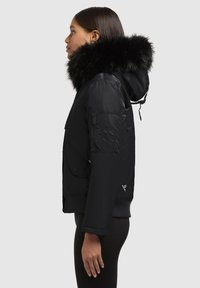 Black insulated jacket with a fur-lined hood, front pockets, a zippered arm pocket, ribbed cuffs, and a fitted design. Smooth texture.
