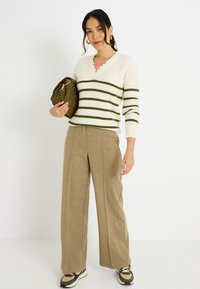 Suéter de punto color crema con rayas verdes, escote en V, cuello festoneado; pantalones anchos color canela; bolso oliva y zapatillas verdes y negras.