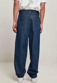 Jeans de mezclilla azul de corte holgado con dos bolsillos traseros, detalles de costura y una cintura alta, combinados con zapatillas blancas.