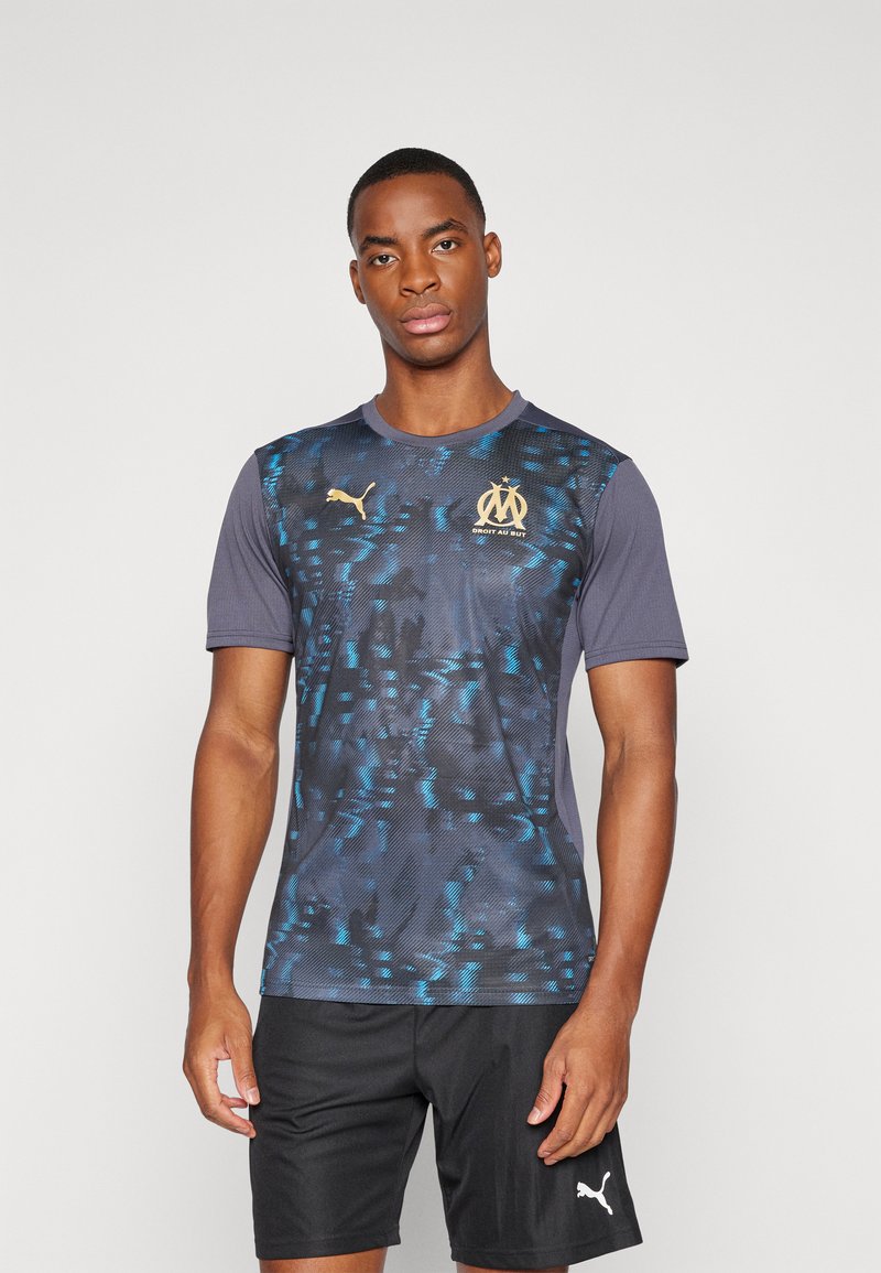 Jersey de manga corta de Puma con un patrón en degradado de azul oscuro a negro, con acentos de logo en dorado y una textura ligera. Usado con pantalones cortos negros.