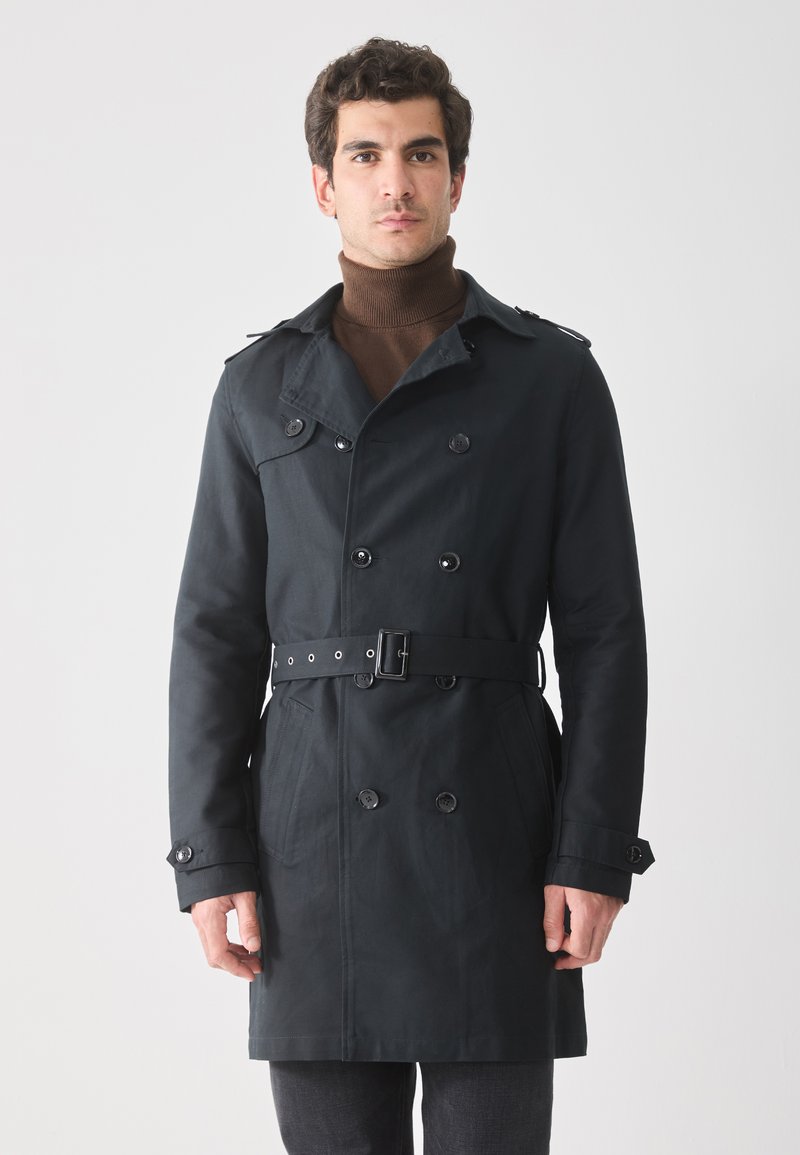 Abrigo negro de trench con botones de doble botonadura, hombreras y cintura con cinturón. Cuenta con mangas largas y bolsillos laterales.