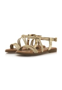 Sandalias trenzadas de oro con suelas planas, que presentan un diseño de tiras y una correa en el tobillo ajustable con hebilla sobre una plantilla marrón suave.