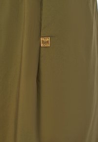 Tessuto verde oliva con una trama liscia presenta un piccolo tag quadrato dorato con la scritta "Manila Grace" sul lato.