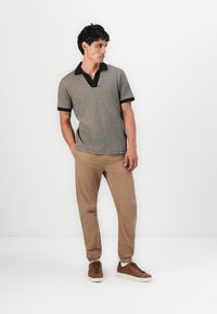 Strikket grå polo med svart krage, kombinert med lyse khaki-bukser og brune sneakers. Modell står mot en ensfarget bakgrunn.