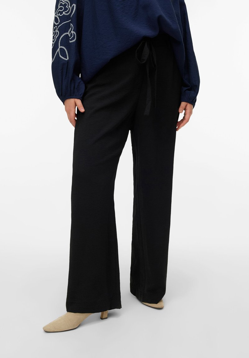 Μαύρο παντελόνι με φαρδύ πόδι από μαλακό ύφασμα με υφή, με ζ ώνη στη μέση και συνδυασμένο με μπεζ ψηλοτάκουνα παπούτσια με μυτερή μύτη.