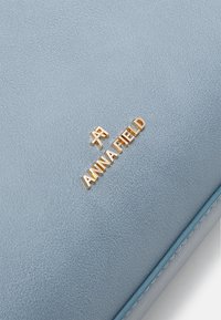 Vaaleansininen synteettisestä nahasta valmistettu lompakko, jossa on teksturoidun pinnan viimeistely. Varustettu kultaisella kohokuvioidulla logolla "ANNA FIELD". Tyylikäs muotoilu, jossa on sileät reunat.