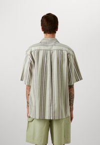 Chemise à manches courtes avec boutonnière en vert clair, ornée de rayures verticales plus foncées, dotée d'un col classique et d'une coupe décontractée.