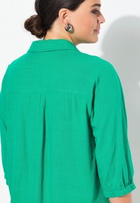 Grøn, struktureret bluse med knap-underskål og 3/4-lange ærmer, med en plissering detaljer bagpå og blødt stof.