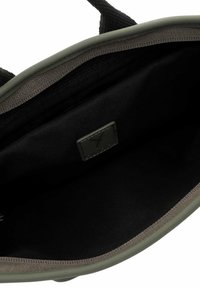 Interno di una borsa in tessuto verde con una fodera nera liscia, dotato di un compartimento con zip e un'etichetta con il marchio su cui è cucita una "X."
