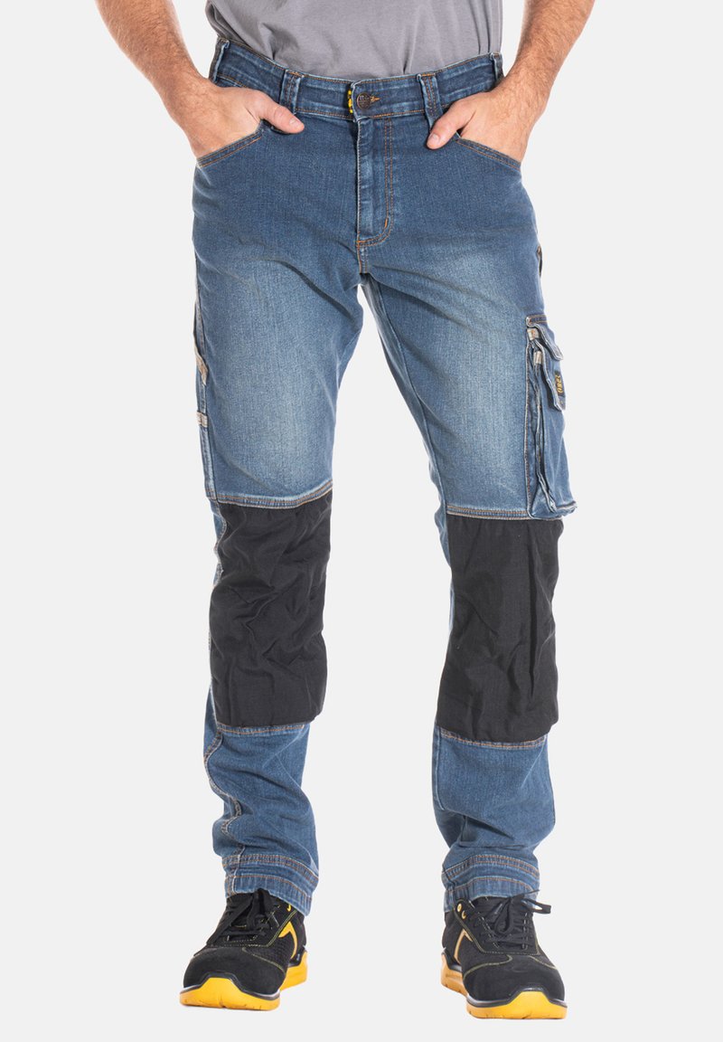 Pantalons cargo en denim avec un lavage bleu clair, des accents en tissu noir aux genoux, plusieurs poches latérales et une poche utilitaire zippée.
