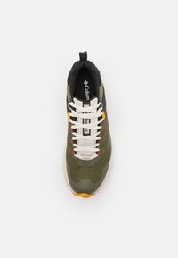 Zielona siateczkowa sneaker z czarnymi akcentami, białymi sznurówkami i gumową podeszwą z pomarańczowym detalem. Widok z góry pokazuje logo na języku i teksturowaną powierzchnię.