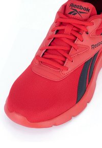 Červená atletická topánka s vrchnou časťou z pletiva a syntetických materiálov, okrúhlym špičkou, viazaním a kontrastnými čiernymi akcentmi po stranách.