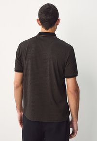 Heren polo met korte mouwen, zwart met een gestructureerd golvend patroon, voorzien van een kraag en contrasterende bies. Gladde stofafwerking.